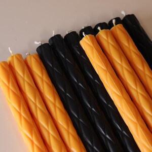 May include: A collection of long, slender taper candles arranged in a row. The candles feature a repeating diamond-shaped embossed pattern along their length and are colored in alternating sections of vibrant orange and solid black wax.
