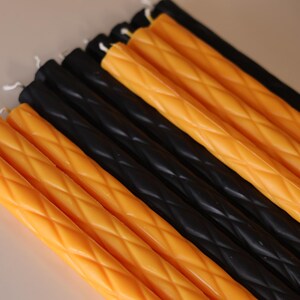 May include: A collection of long, slender taper candles arranged in alternating rows of vibrant orange and solid black. Each candle features a distinct diamond-shaped lattice texture embossed along its length, topped with a small white cotton wick.