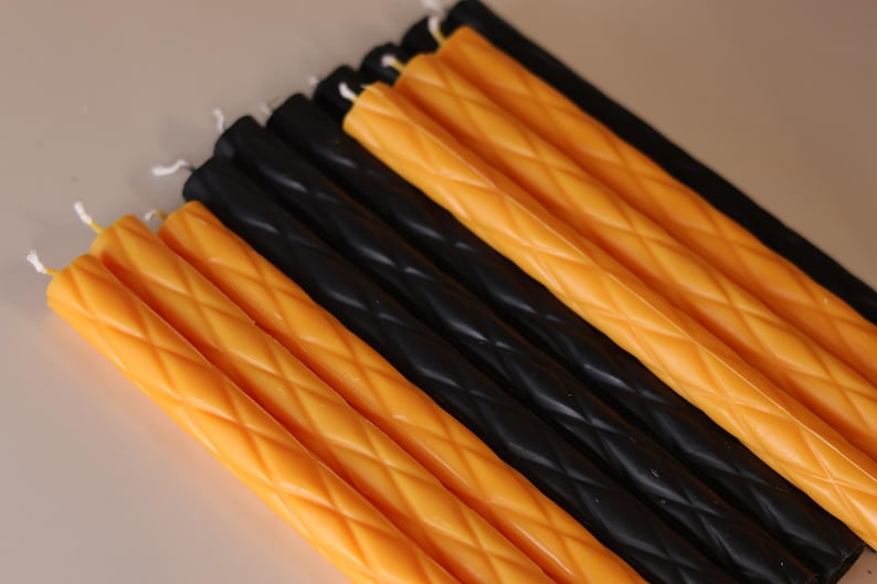 May include: A collection of long, slender taper candles arranged in alternating rows of vibrant orange and solid black. Each candle features a distinct diamond-shaped lattice texture embossed along its length, topped with a small white cotton wick.