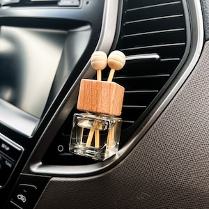 May include: A small glass car air freshener with a wooden top and two wooden sticks. The air freshener is hanging from the air vent in a car.