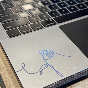May include: A silver laptop computer with a blue and purple holographic sticker of a stylized rose on the top right corner of the trackpad.