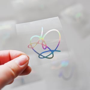 May include: A clear sheet of vinyl with a holographic iridescent heart-shaped design. The design is a stylized, abstract heart shape.