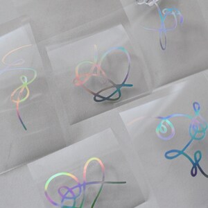 May include: A set of holographic stickers featuring different designs, including hearts, flowers, and abstract shapes. The stickers are on a clear background and are perfect for adding a touch of sparkle to any project.