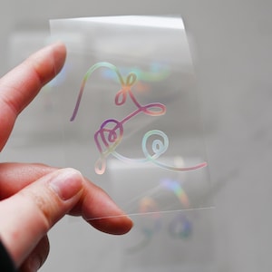 May include: A clear sheet with a holographic iridescent sticker of a stylized heart design.