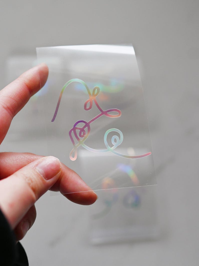 May include: A clear sheet with a holographic iridescent sticker of a stylized heart design.