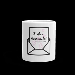 May include: White ceramic mug with a black and white illustration of an envelope with a pink heart inside. The text on the envelope reads "Te Amo Mamacita! You make me happy."