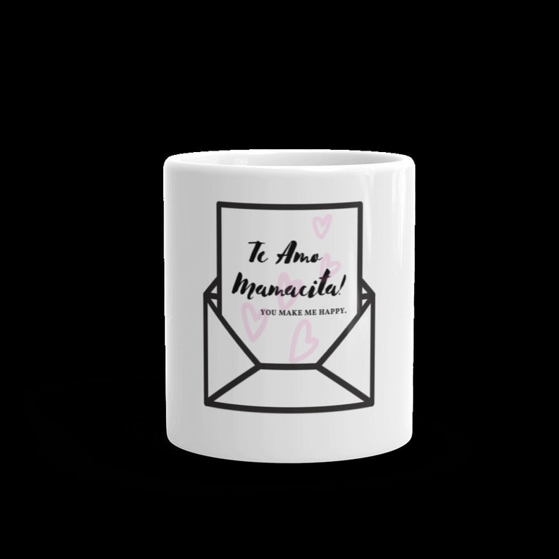 May include: White ceramic mug with a black and white illustration of an envelope with a pink heart inside. The text on the envelope reads "Te Amo Mamacita! You make me happy."