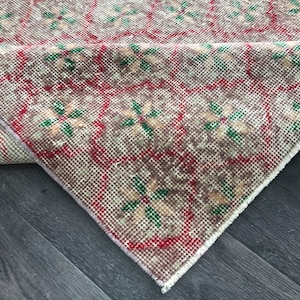 Puede incluir: Una alfombra vintage con un patrón geométrico en tonos rojos, verdes y beige. La alfombra está doblada por la mitad, mostrando el reverso de la alfombra.