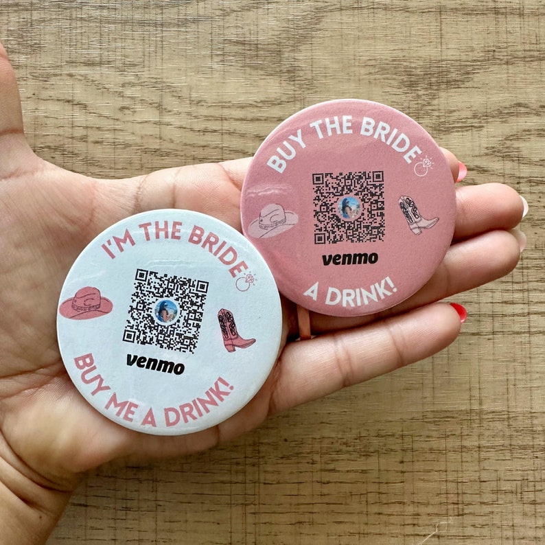 Peut inclure: Deux boutons ronds roses avec un code QR, le texte "Buy the Bride" et "I'm the Bride", et les mots "Venmo" et "A Drink!" imprim&eacute;s dessus.