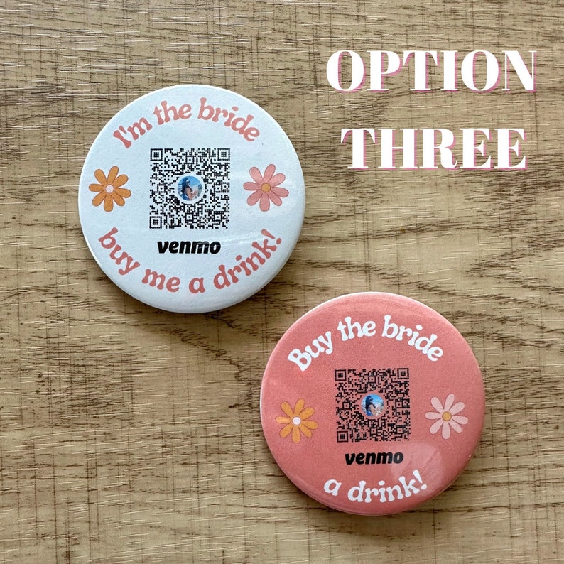 Peut inclure: Deux boutons ronds avec un code QR, des fleurs et le texte "I'm the bride buy me a drink!" et "Buy the bride a drink!" avec le mot "venmo" sur les deux. Les boutons sont blancs et roses.
