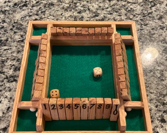 May include: A wooden game board with a green felt playing surface. The board has a wooden frame and a set of numbered wooden blocks. There are two dice on the board, one with the number 3 and the other with the number 5.