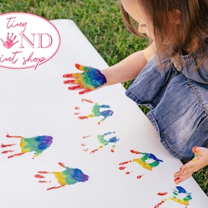 May include: A child makes rainbow handprints on a white surface. The text "tiny HAND print shop" is visible in the top left corner of the image.