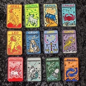 May include: Twelve colorful embroidered patches featuring the astrological signs of the zodiac. Each patch is rectangular and has a white border. The signs are Aries, Taurus, Gemini, Cancer, Leo, Virgo, Libra, Scorpio, Sagittarius, Capricorn, Aquarius, and Pisces.