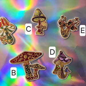 May include: Five embroidered iron-on patches featuring different mushroom designs. The patches are on a rainbow iridescent background. The patches are labeled A through E.