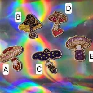 May include: Six embroidered iron-on patches featuring different mushroom designs. The patches are in various colors, including purple, pink, gold, and white. The patches are perfect for adding a whimsical touch to clothing, bags, or other accessories.