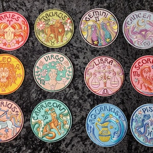 May include: Twelve embroidered iron-on patches featuring the astrological signs of the zodiac. Each patch is circular and features a colorful design with the name of the sign and its symbol.