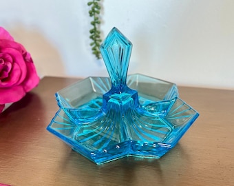Op de afbeelding: Een blauwe glazen serveerschaal met een centrale handgreep en drie aparte compartimenten. De schaal heeft een stervormig patroon.