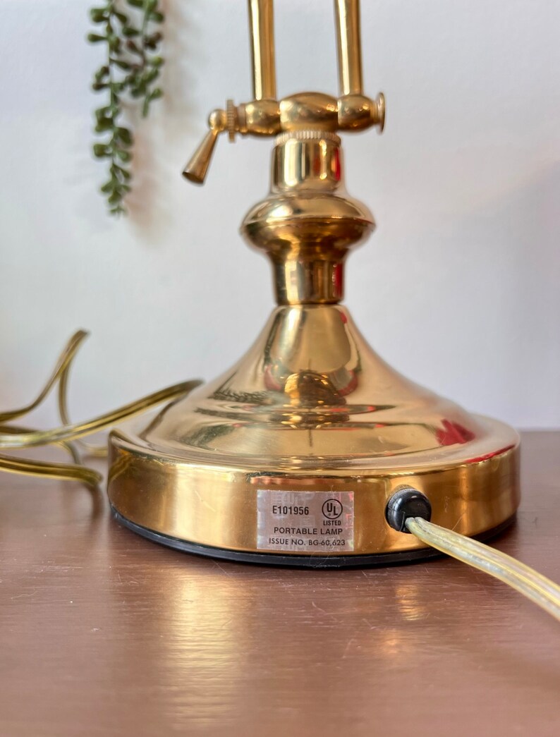 Może przedstawiać: Złota przenośna lampa z czarnym kablem i etykietą UL. Etykieta zawiera napis "E101956 LAMPA PRZENOSNA NUMER ZESPOŁU 8G-60,023".