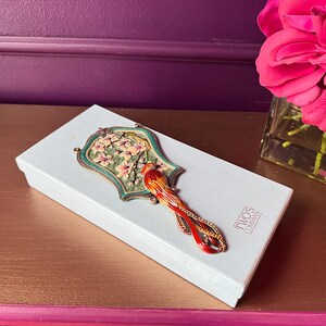 May include: A white box with a decorative bird-shaped mirror on top. The mirror has a green and gold frame with a floral design and a red and orange bird. The box has the text "TWO'S COMPANY".