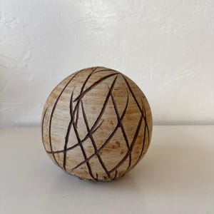 May include: A spherical, decorative object with a light brown, textured surface. Dark brown lines intersect across the sphere, creating a geometric pattern. The object is likely ceramic or stone and sits on a white surface.