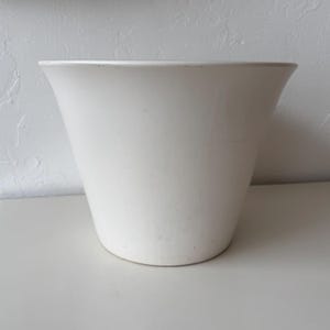 May include: A white ceramic plant pot with a flared top and a gently tapering body. The pot has a smooth, matte finish. Suitable for indoor or outdoor use, the design is simple and modern, suitable for various plants.
