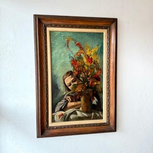 以下が含まれることがあります： 女性と色とりどりの花瓶が描かれた、ヴィンテージの額入り油絵。アートワークは、彫刻が施されたディテールが施された濃い木製のフレームです。花は赤、黄色、オレンジの混合で、ターコイズの背景に設定されています。