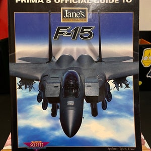 May include: A Prima's Official Guide to Jane's F-15 Combat Simulations book cover featuring a black F-15 fighter jet flying against a blue sky with white clouds. The book title is in white text with a red and white logo for Prima's Secrets of the Game.