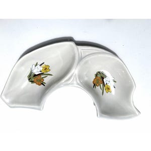 May include: A white ceramic divided serving dish with a curved, crescent-like shape. The dish features two distinct concave sections, each decorated with a floral illustration of white, yellow, and orange crocus flowers with green stems.