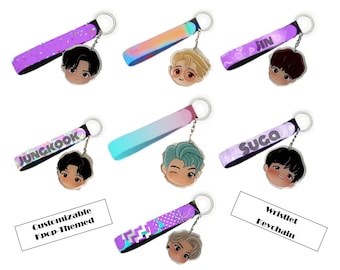May include: A set of customizable wristlet keychains featuring different K-pop idols. Each keychain has a purple, iridescent, or glittery strap with a cartoon image of a K-pop idol. The text "Customizable Kpop-Themed" and "Wristlet Keychain" are visible in the image.