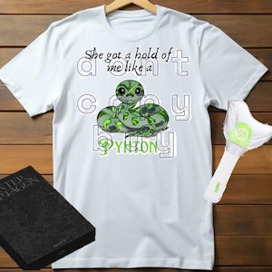 Puede incluir: Camiseta blanca con un gráfico de serpiente verde y el texto "She got a hold of me like a cozy python".