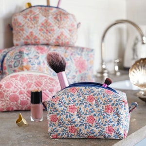 Könnte beinhalten: Vier gequiltete Kosmetiktaschen mit floralem Muster in Rosa, Weiß und Blau mit einer Kosmetiktasche mit floralem Muster in Rosa und Weiß im Vordergrund. Die Kosmetiktasche im Vordergrund enthält zwei Make-up-Pinsel.