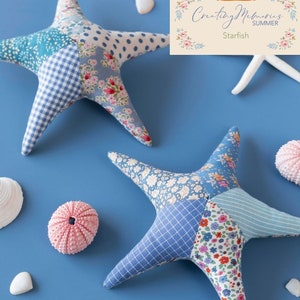 Può includere: Due stelle marine in tessuto patchwork blu e bianco su uno sfondo blu. Le stelle marine sono fatte a mano e presentano una varietà di motivi floreali e geometrici. Il testo "Tilda Creating Memories Summer Starfish" è visibile nell'angolo in alto a destra dell'immagine.