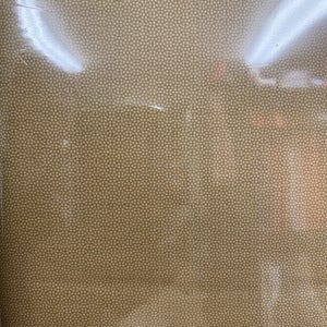 Pode incluir: Close-up de um tecido bege tecido com um pequeno padrão repetitivo. O tecido tem uma aparência texturizada e uma cor neutra, adequado para várias aplicações. A imagem está ligeiramente desfocada.