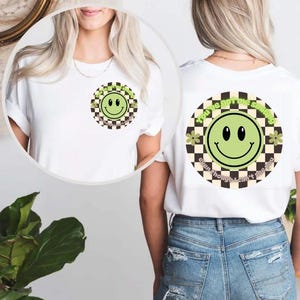 Op de afbeelding: Wit T-shirt met een groene smiley-afbeelding op een zwart-wit geruite achtergrond. De tekst "You've got the smile even though I can't see you" staat rond de afbeelding.