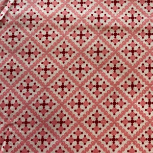 Peut inclure: Un tissu textile présentant un motif géométrique répétitif en losanges dans des tons de rose clair et de rouge foncé. Le design se compose de formes en losange interconnectées soulignées par de petits points, avec un motif central en croix.