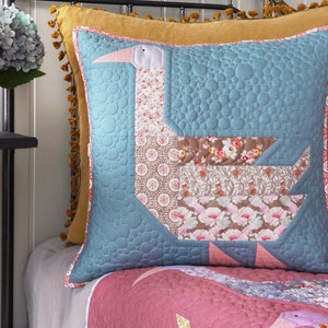Può includere: Un cuscino a forma di oca in patchwork blu e rosa con un design trapuntato. Il cuscino è su un copriletto rosa e bianco.