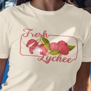 May include: A white t-shirt with a pink rectangle graphic featuring the text "Fresh Lychee" and a drawing of lychees.