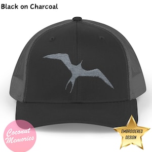Może przedstawiać: Czarna czapka typu trucker na węglu drzewnym z szarym haftowanym wzorem ptaka. Czapka ma siatkowy tył i zakrzywiony daszek. Tekst "Black on Charcoal" znajduje się u góry obrazu. Czapka ma logo "Coconut Memories" i złotą gwiazdę z napisem "Embroidered Design".