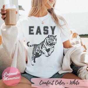 Pu&ograve; includere: Maglietta bianca con la parola "EASY" stampata in lettere nere e un'immagine di tigre bianca e nera. La maglietta &egrave; indossata da una persona.