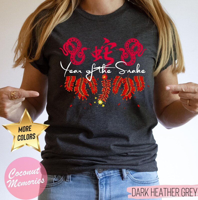 以下が含まれることがあります： ダークヘザーグレーのTシャツに、赤い中国語の「蛇」の文字と「蛇の年」の文字が書かれています。デザインには、赤い爆竹と赤い蛇も含まれています。