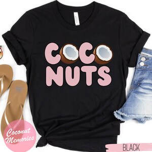 May include: Black t-shirt with the text "COCONUTS" in pink bubble letters. Three brown coconuts with white insides are behind the "CO" in the text.