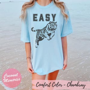 Pu&ograve; includere: Una maglietta blu chiaro con la parola "EASY" stampata in lettere nere e un'immagine di tigre bianca e nera. La maglietta &egrave; realizzata in un materiale morbido e confortevole.