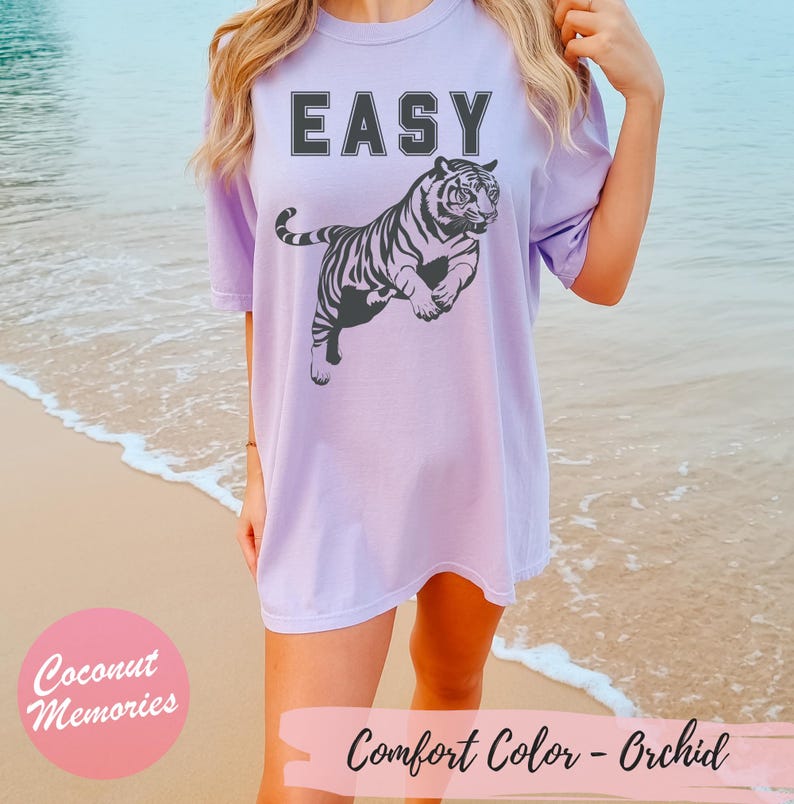 Pu&ograve; includere: Una maglietta oversize color lavanda con la parola "EASY" stampata in nero e una grafica di tigre in bianco e nero. La maglietta ha una vestibilit&agrave; rilassata e un collo rotondo.