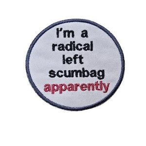 May include: Embroidered patch with the text "I'm a radical left scumbag apparently" in black and red. The patch is circular with a light gray background and a dark blue border. The text is centered.