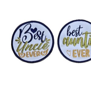 May include: Two white embroidered iron-on patches with navy blue borders. One patch says "Best Uncle Ever" in gold and orange lettering with a heart. The other patch says "Best Auntie Ever" in gold lettering with two hearts.