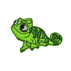 May include: A green embroidered patch featuring a cartoon chameleon with large, expressive eyes. The chameleon has a curled tail and dark green stripes on its back. The patch is designed to be ironed on or sewn onto fabric.