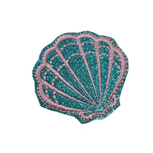 May include: A teal blue glitter seashell with a pink outline. The seashell is embroidered with a detailed design.