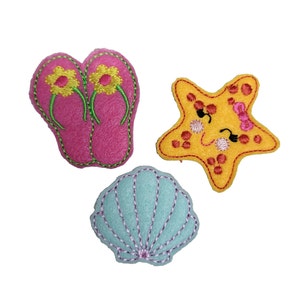 May include: Three felt appliques in a summer theme. A pair of pink flip flops with green straps and yellow flowers, a yellow starfish with a pink bow and sunglasses, and a light blue seashell.