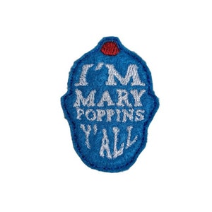 May include: A blue felt patch with white embroidered text that reads "I'M MARY POPPINS Y'ALL". The patch has a unique shape with a red circular accent at the top. The patch is on a white background.