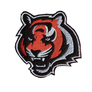 May include: Embroidered iron-on patch featuring a black and white tiger head with orange stripes. The tiger has a fierce expression with a wide open mouth and sharp teeth.
